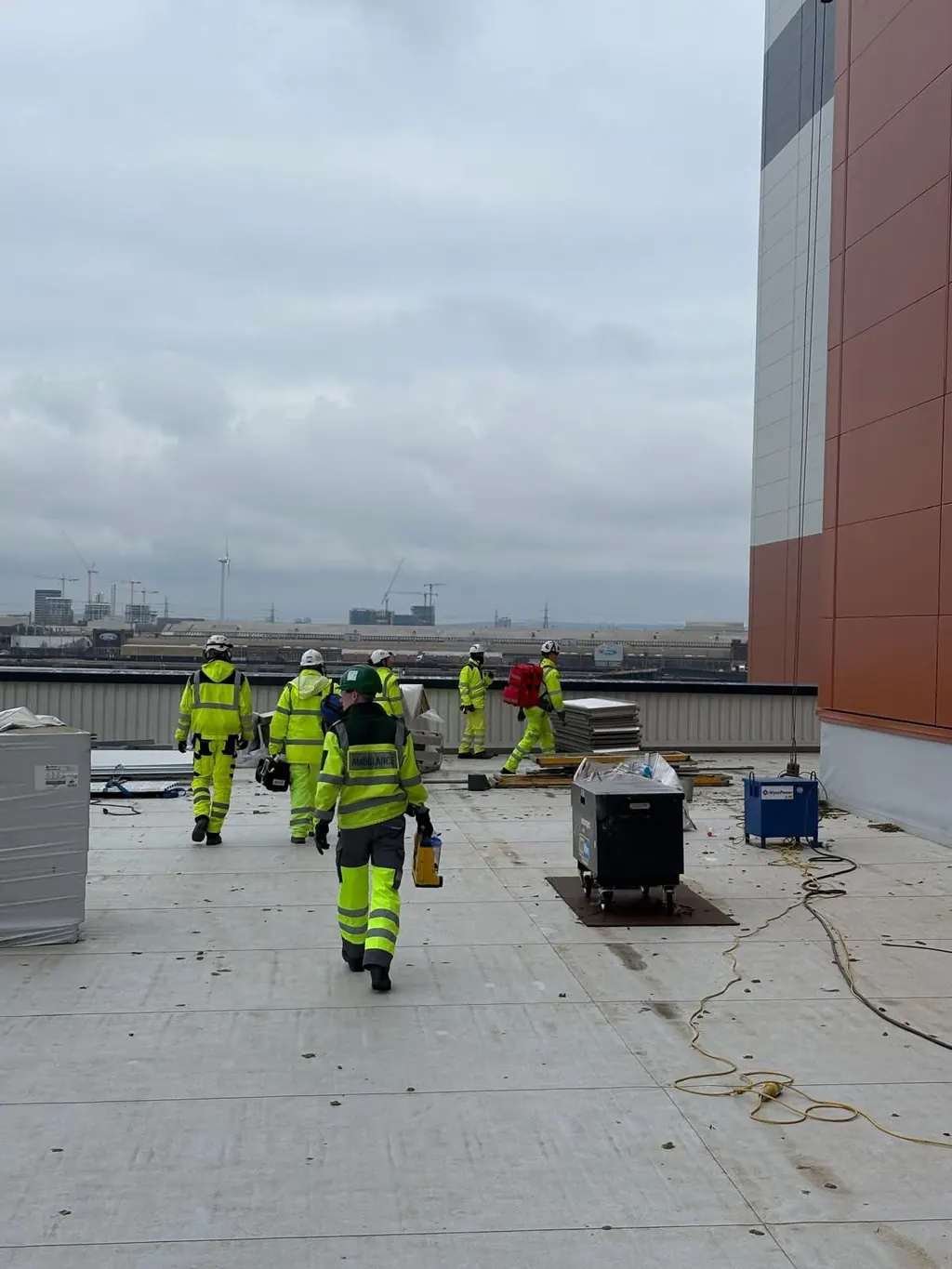 LightMed rescue team medic walking across a rooftop construction site with high-visibility construction workers.