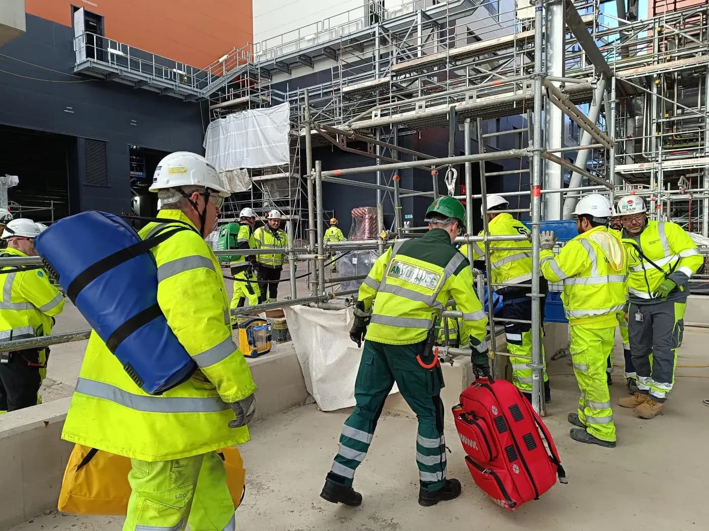 LightMed rescue team medic carrying a response bag on a construction site beside scaffold and high-visibility workers.