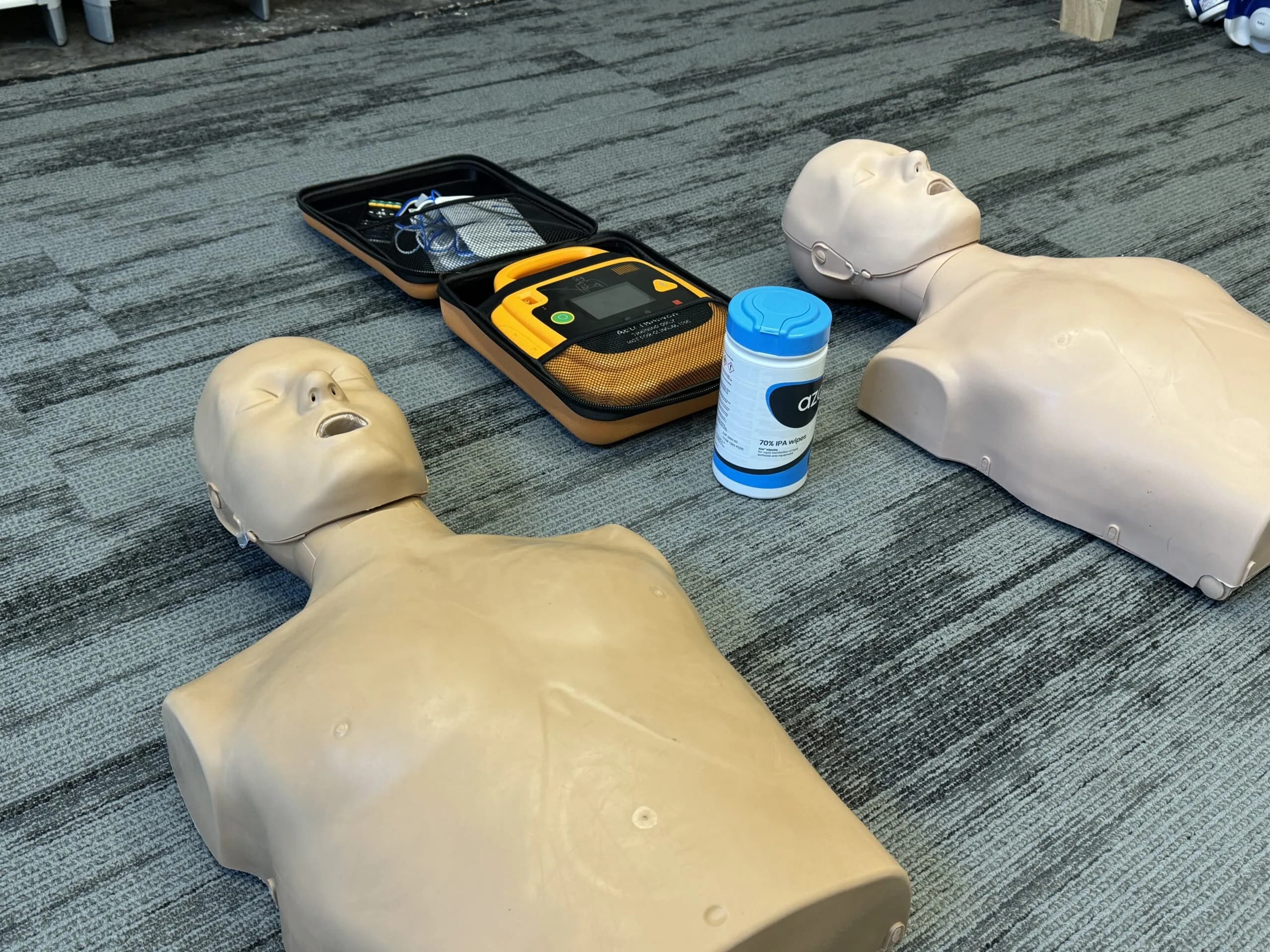 CPR training manikins laid out with an AED trainer and cleaning wipes during a LightMed first aid training session.